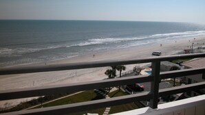 A beach view from a balcony with a railing, ocean, and a parking area with a red car. - 7th Floor End Unit - Right on the Beach (Daytona Beach)