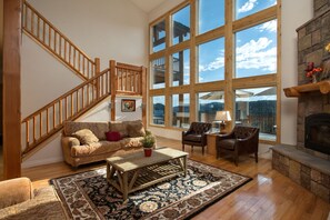 Un salon spacieux avec un escalier en bois, de grandes fenêtres, une cheminée et un coin salon confortable.