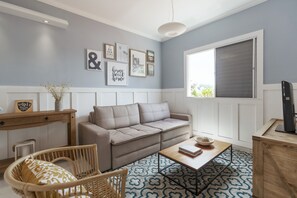A living room with a beige sofa, a wooden coffee table, a wicker chair, and a patterned rug.