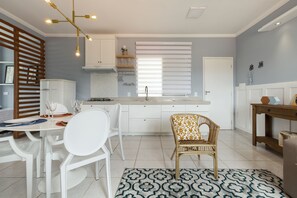 A modern kitchen with white cabinets, a dining area with white chairs, and a patterned rug.