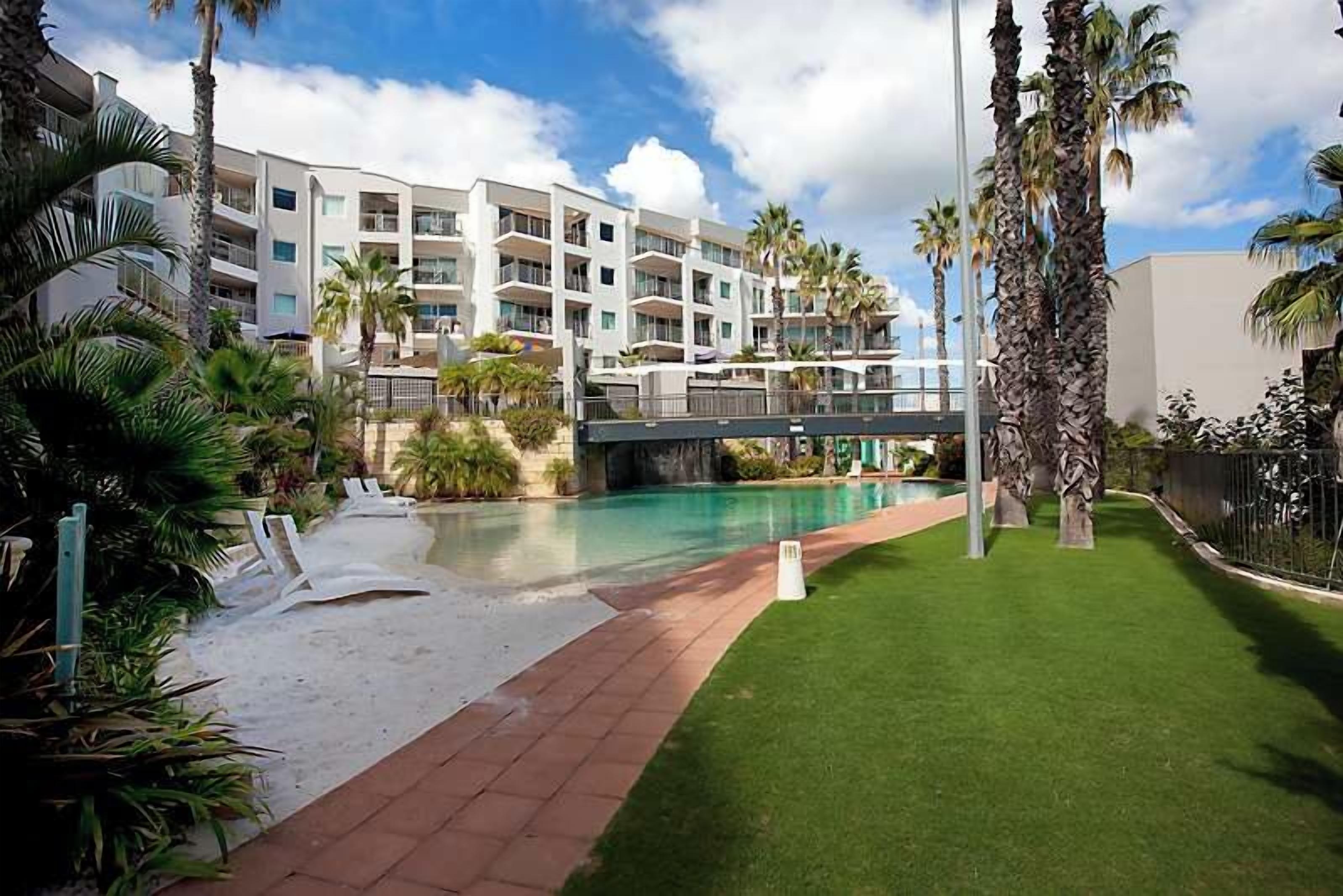 Un hôtel moderne doté d’une piscine, de palmiers et offrant une vue sur un ciel dégagé.