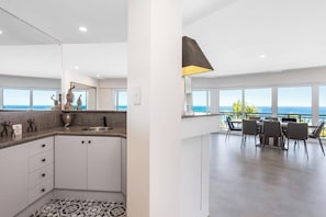 A modern kitchen with a view of the ocean, a dining area with a table and chairs, and a large window overlooking the sea.