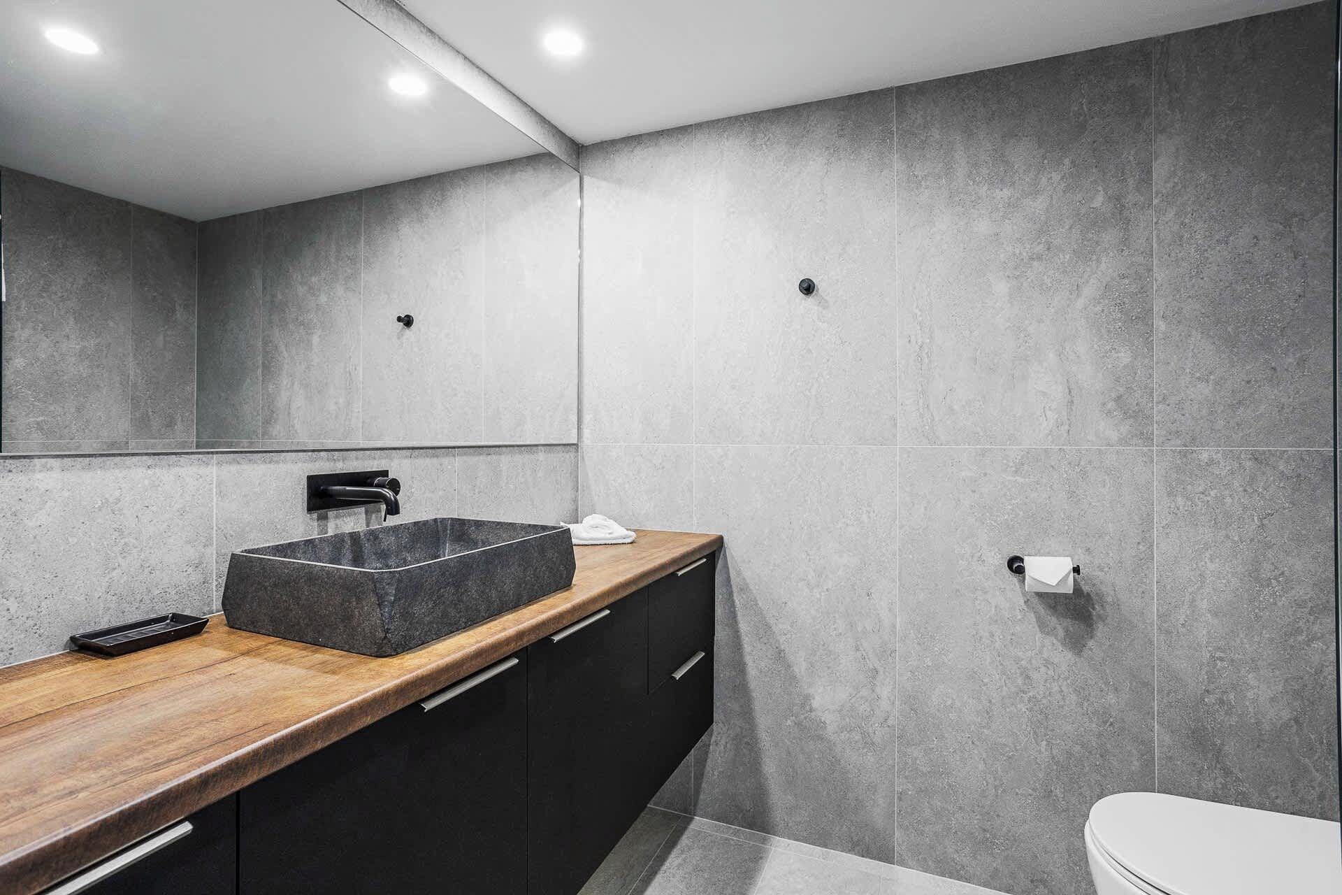 A modern bathroom with a rectangular sink, dark cabinets, and a wooden countertop.