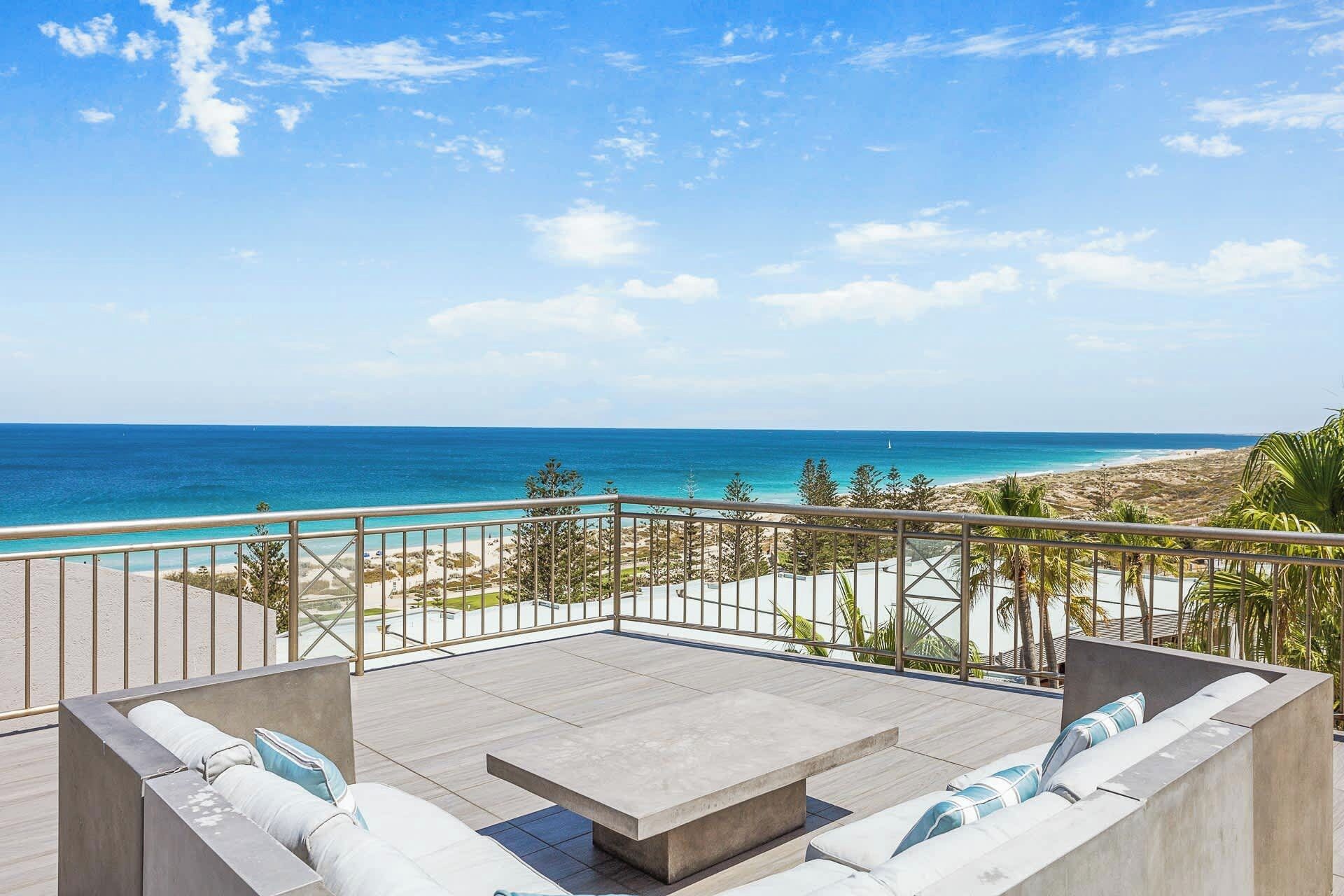 Ein Balkon mit Blick auf das Meer und den Strand, ausgestattet mit einer Beton-Sitzgruppe und Kissen.