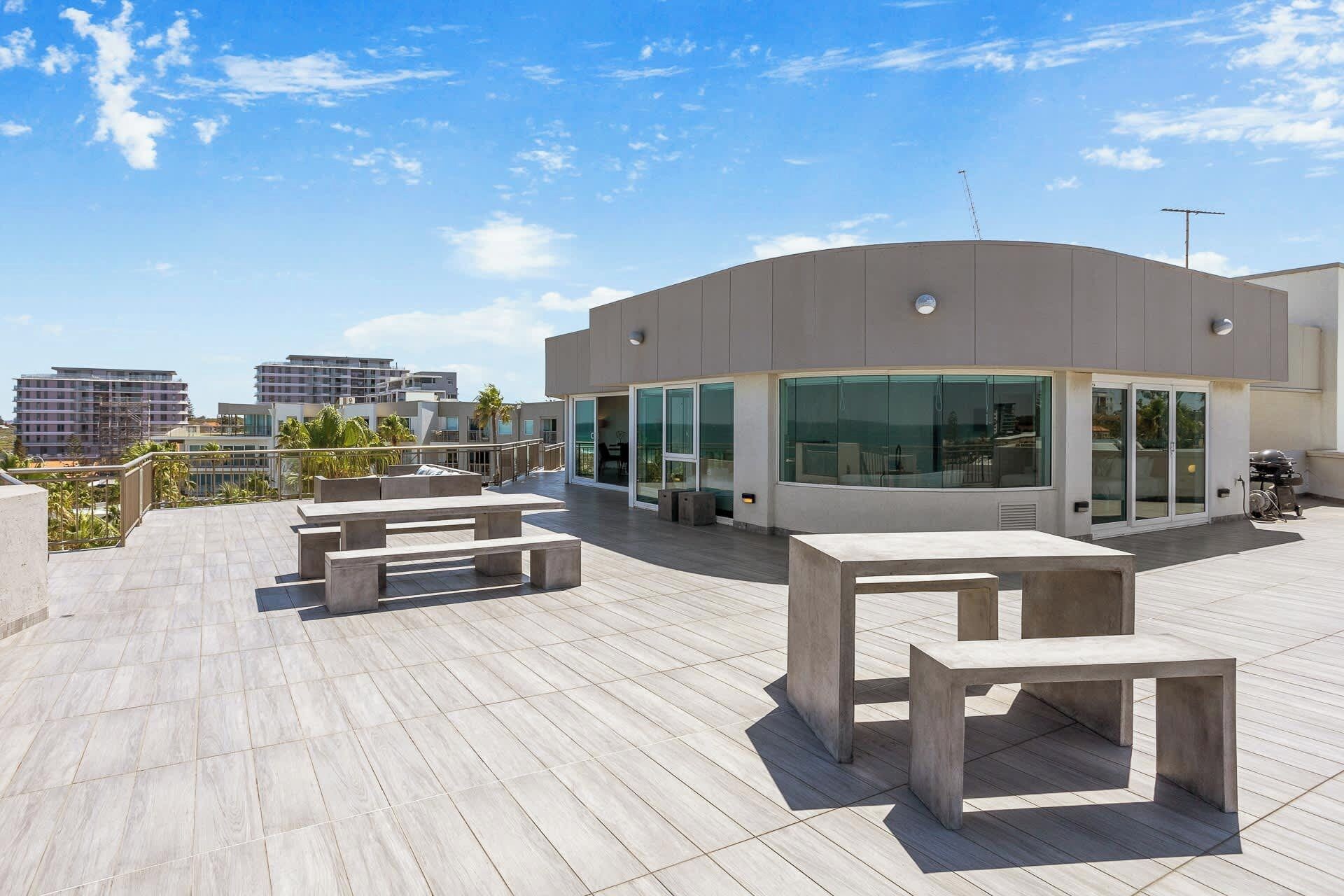 A modern building with large windows and a flat roof terrace with concrete benches.