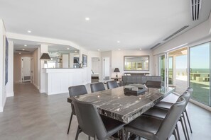 A modern dining area with a marble table and black chairs, a kitchen with a glass counter, and a balcony with a view. - Apartment M601 - Spectacular Beachfront Penthouse! (Scarborough)
