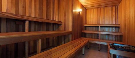 Un sauna avec des bancs et des murs en bois, un banc muni d’un plateau et un luminaire au plafond.