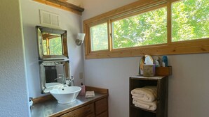 Un baño con armarios de madera, un lavabo blanco, un espejo y una ventana con vistas a árboles.