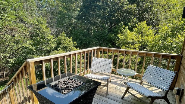 Una terraza de madera con una mesa de hogar a prueba de fuego color negro, dos sillas de mimbre y una mesa de vidrio.