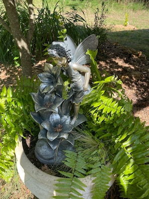 Garden statue of a fairy-like figure sits amidst lush greenery in a well-maintained garden area.
