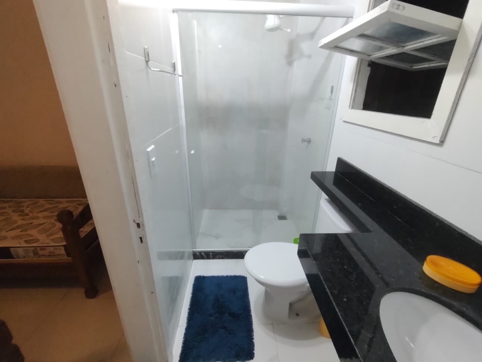 Un baño con cabina de ducha de vidrio, inodoro blanco, encimera negra y jabonera amarilla.