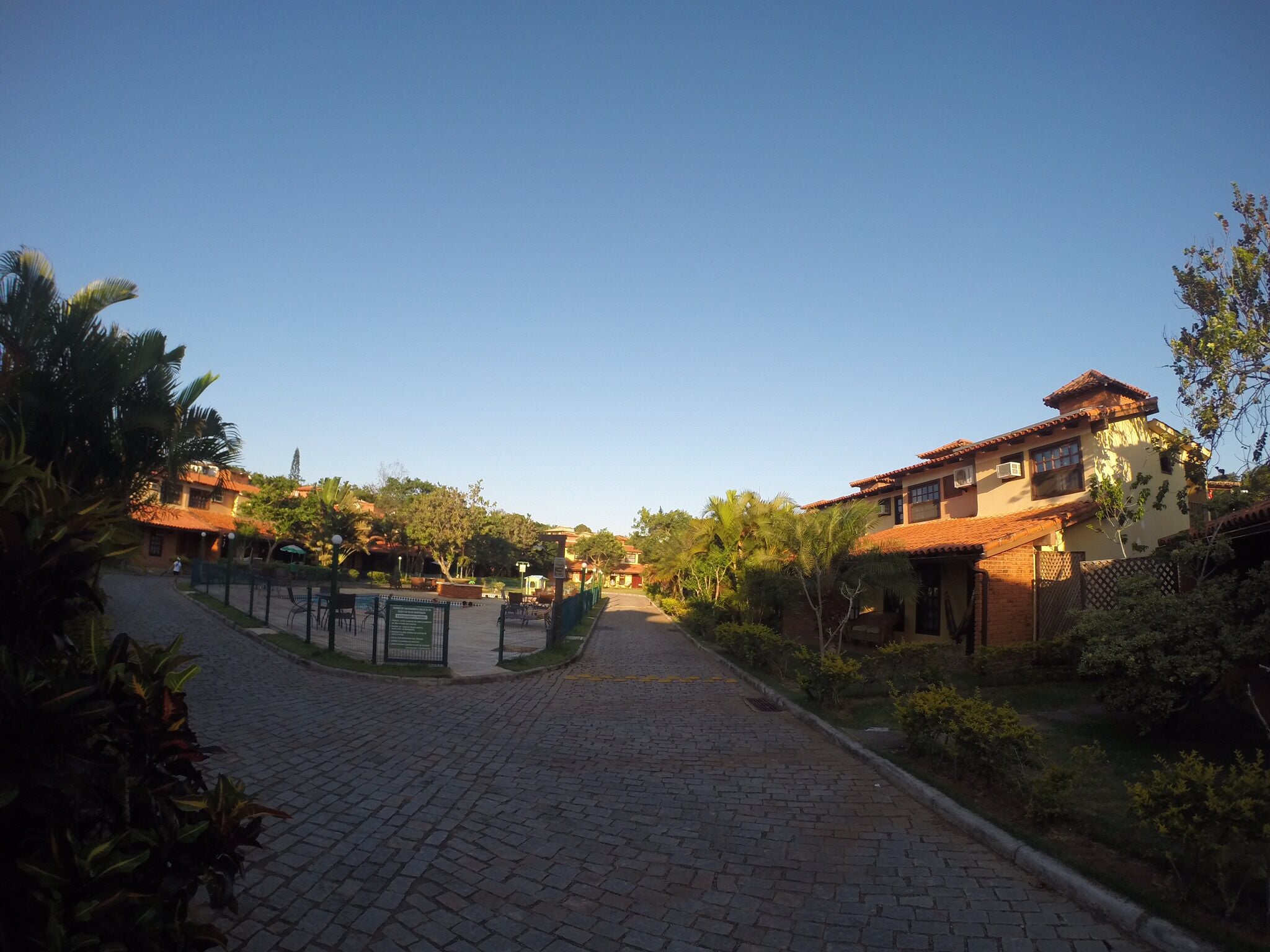 A paved pathway leading to a building with a tiled roof, surrounded by greenery and a clear sky.