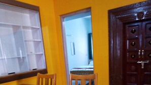 Un comedor con una mesa y sillas de madera, una ventana con persianas y una puerta con un panel decorativo.