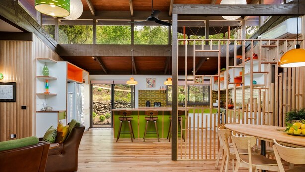 Una cocina moderna con piso de madera, un comedor con sillas de madera y una barra con taburetes.