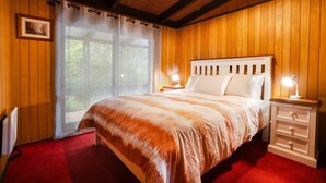 Une chambre avec un mur lambrissé en bois, un lit avec une literie blanche, une moquette rouge et une table de chevet avec une lampe.