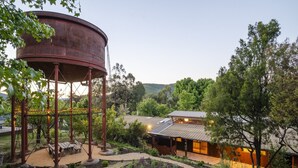 Un edificio rústico con un depósito de agua, terraza de madera y senderos en el jardín.