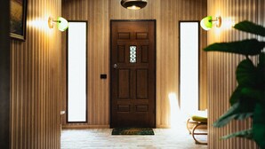 Un pasillo revestido de madera con una puerta de madera oscura, dos luces fijadas a la pared y una planta pequeña en primer plano.