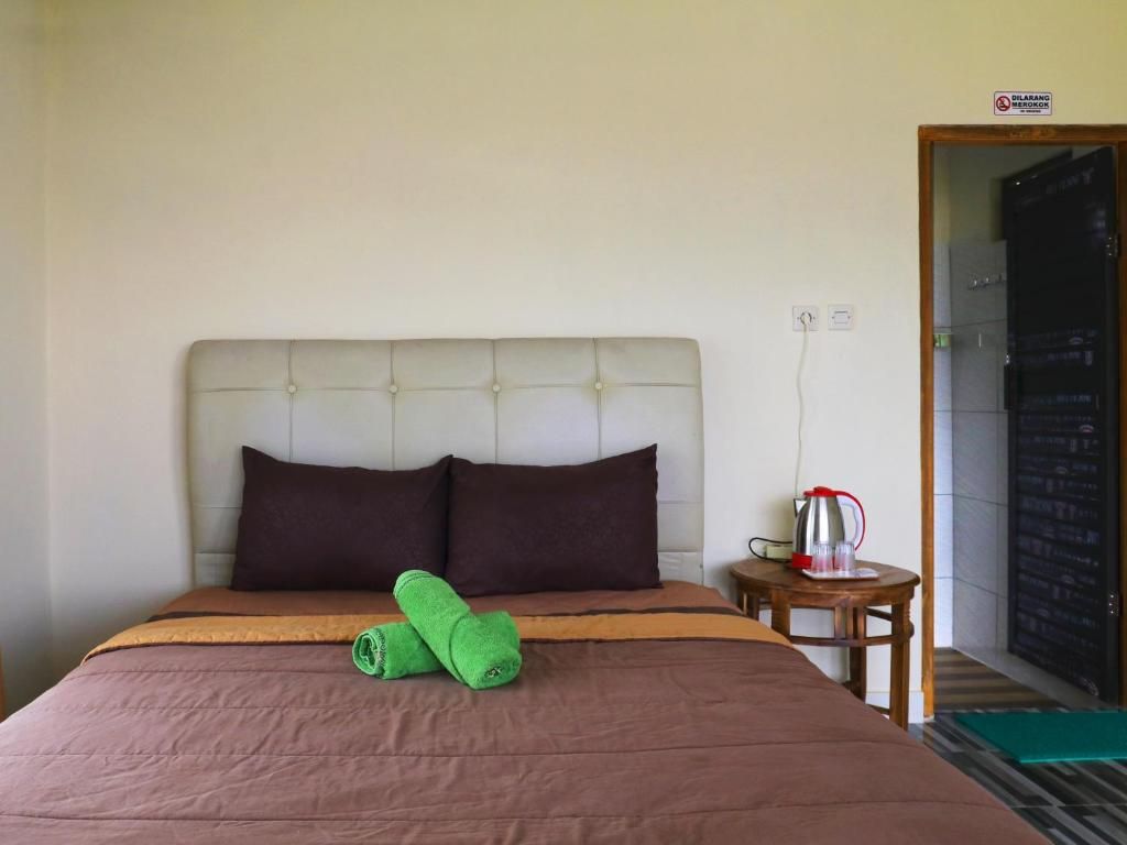 A hotel room with a bed, two pillows, a green towel, a coffee pot, and a small table.