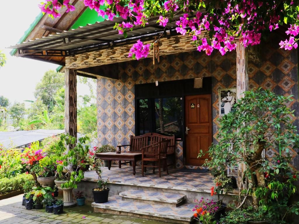 A covered porch with a wooden bench and a door, surrounded by potted plants and flowers.
