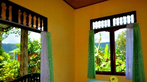 A room with a bed, a window with curtains, and a view of greenery outside. - Dajan Buyan Homestay (Bedugul)