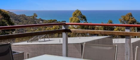 Una terraza con vista al océano, mobiliario exterior y baranda.