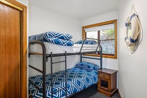 A bunk bed room with a window, a small wooden cabinet, and a life preserver hanging on the wall.