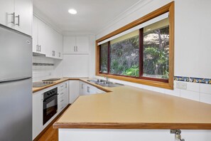 A kitchen with white cabinets, a wooden countertop, a built-in oven, and a window with a view of greenery.