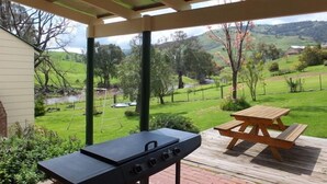 Un porche cubierto con una parrilla y una mesa de picnic, con vistas a un paisaje verde con árboles y colinas.