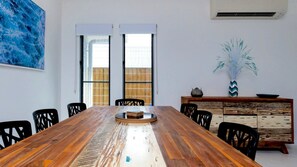 Een vergaderruimte met een lange houten tafel, zwarte stoelen, een whiteboard en een decoratieve kast met een plant.