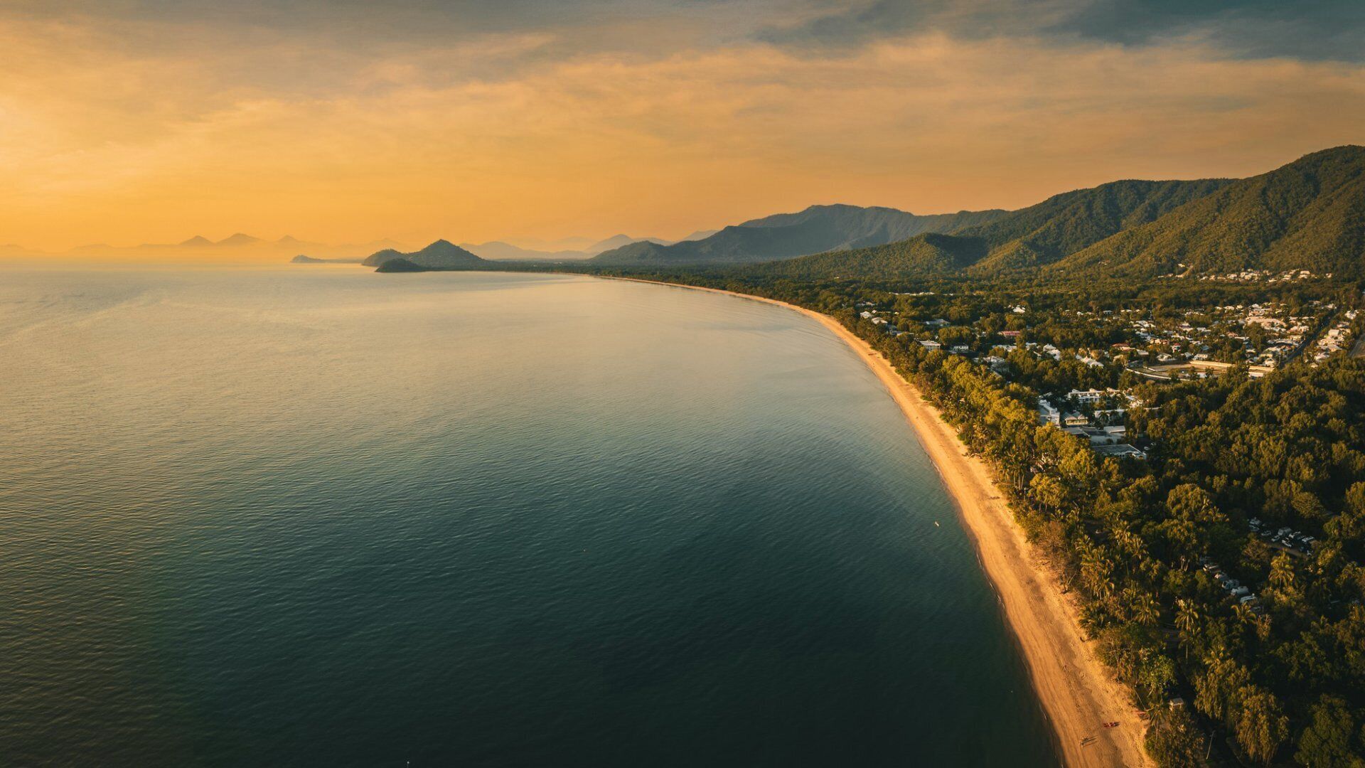 Un paisaje costero con una playa, colinas boscosas y una isla distante.