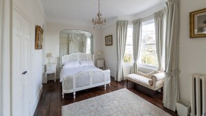 A bedroom with a four-poster bed, a sitting bench, a mirror, a chandelier, and a window with curtains. - Georgian Manor With Panaromic Sea Views (Torquay, Devon)