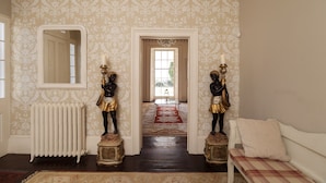 A hallway with patterned wallpaper, a radiator, a mirror, a chandelier, and a bench with a cushion. - Georgian Manor With Panaromic Sea Views (Torquay, Devon)
