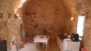 A stone-walled room with a white table and chairs, a small kitchenette, and a blue sofa with a red pillow. - Old Tower-House in Mani peninsula (LAGIA)