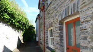 A narrow alleyway with a stone building featuring a red door and a window. - COMFORTABLE, TRANQUIL, HOUSE ON RIVER TEIFI  LARGE GARDEN, CENTRAL, FREE PARKING (Cardigan)
