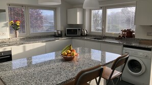 A modern kitchen with granite countertops, a central island with a fruit bowl, a built-in dishwasher, and a washing machine. - COMFORTABLE, TRANQUIL, HOUSE ON RIVER TEIFI  LARGE GARDEN, CENTRAL, FREE PARKING (Cardigan)