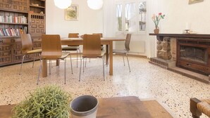 A cozy living room with a wooden dining table, chairs, a bookshelf, a fireplace, and a large window with curtains. - Beautiful private villa for 7 people with A/C, WIFI, hot tub, TV and patio (Cambrils)
