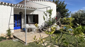 A white building with a blue door and window shutters, a covered patio with a table and chairs, and a small garden area. - Beautiful private villa for 7 people with A/C, WIFI, hot tub, TV and patio (Cambrils)