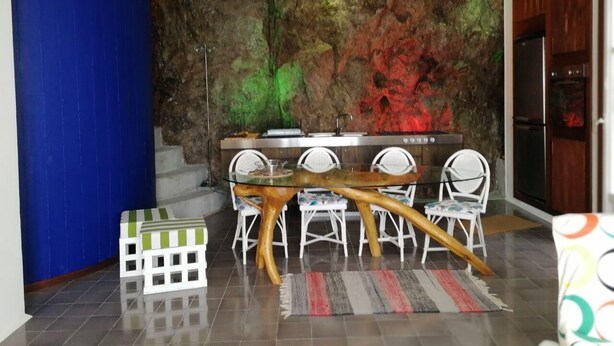 Una cocina moderna con una isla central, sillas blancas y una pared azul decorativa.