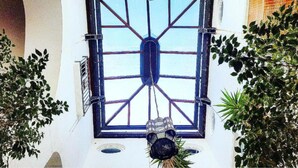 A courtyard with a large central window, surrounded by greenery and a hanging lantern. - Henry House (Sorrento)