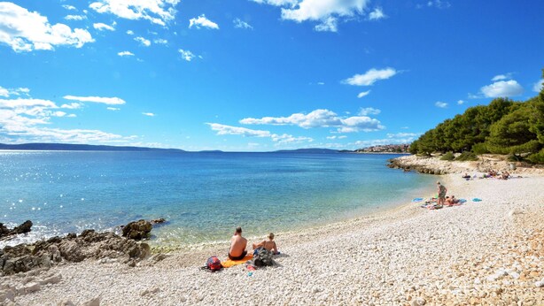 Ein Kiesstrand mit klarem, blauem Wasser und einigen Personen, die sich sonnen.
