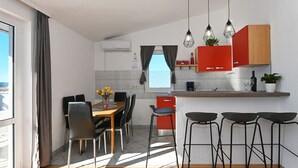 Eine moderne Küche mit roten Schränken, ein Essbereich mit einem Holztisch und Stühlen sowie eine Bar mit Hockern.