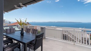 Ein Balkon mit Tisch und Stühlen, der Blick auf das Meer hat.