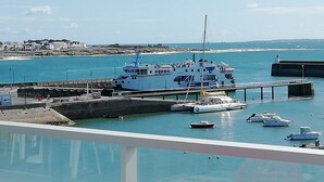 Un muelle de transbordador con un ferry grande, embarcaciones más pequeñas y un espigón que se adentra en el agua.