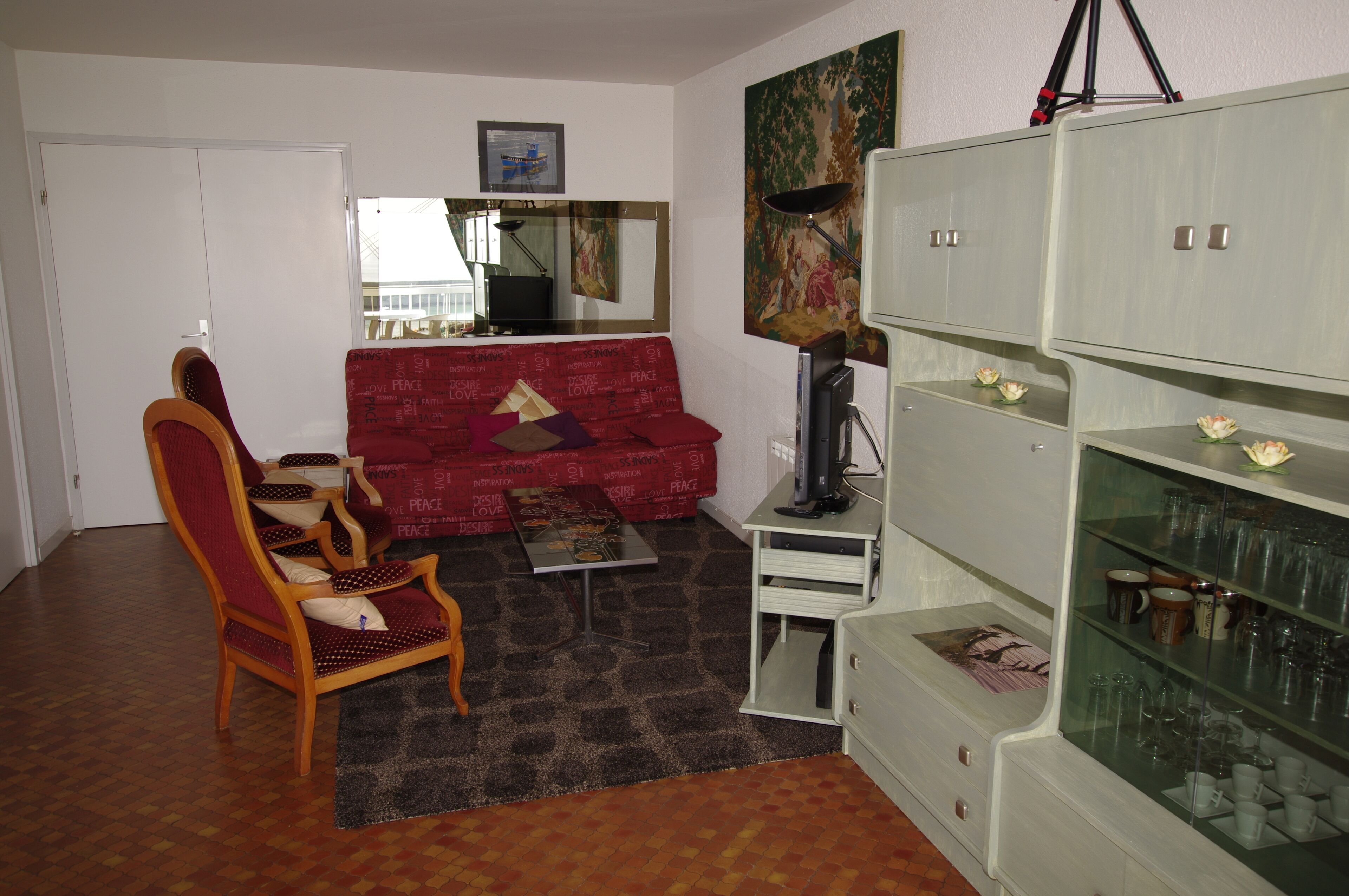 A living room with a red sofa, a wooden chair, a glass coffee table, and a cabinet with glass doors.