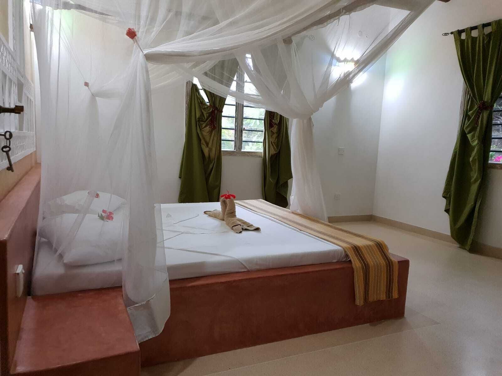 Ein Schlafzimmer mit einem Himmelbett, einer hölzernen Bank und grünen Vorhängen.