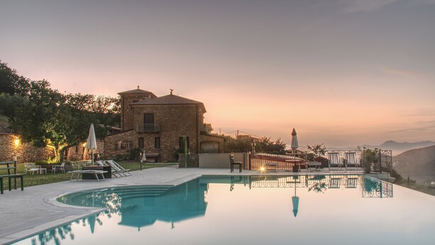 A serene pool area with a stone building, outdoor seating, and a view of distant mountains. - Farmhouse with infinity pool: A unique experience-Onice (castellabate)