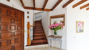 Eine Holzt Treppe mit Handlauf, eine Holztür, ein kleiner Tisch mit Blumenvase und ein Spiegel an der Wand.
