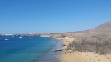 Uma praia com águas azul-claras, areal arenoso e colinas rochosas ao fundo.