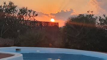 Piscina com vista para o pôr do sol, cercada por palmeiras e bambu.