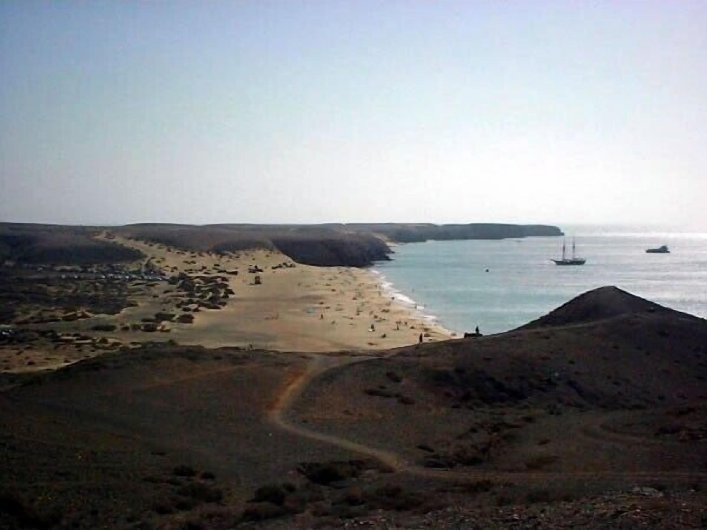Un paysage côtier avec une plage, un bateau sur l’eau et un terrain vallonné.